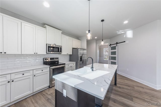 kitchen with stainless steel appliances, an island with sink, a barn door, and white cabinets