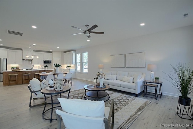 living room featuring sink, light hardwood / wood-style flooring, and ceiling fan