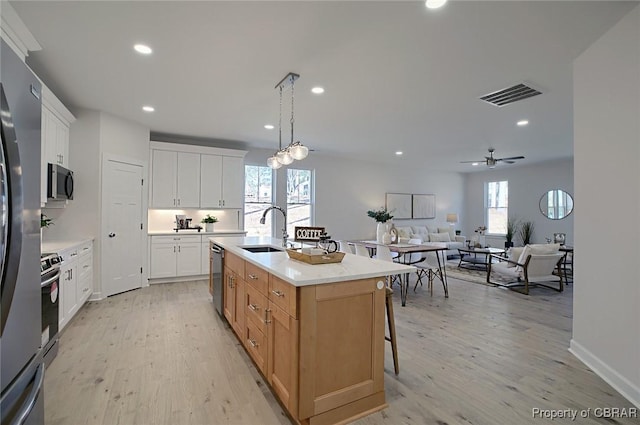 kitchen with sink, appliances with stainless steel finishes, a kitchen island with sink, white cabinetry, and decorative light fixtures