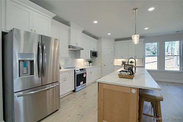 kitchen featuring an island with sink, sink, white cabinets, stainless steel appliances, and light stone countertops