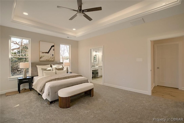 bedroom with ceiling fan, light colored carpet, ensuite bathroom, and a tray ceiling