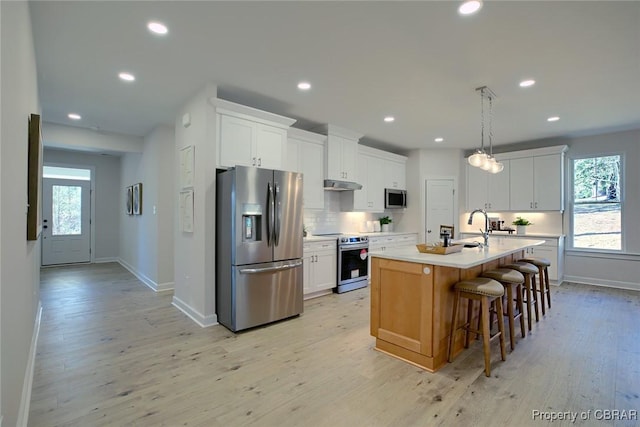 kitchen with appliances with stainless steel finishes, an island with sink, white cabinets, a healthy amount of sunlight, and backsplash