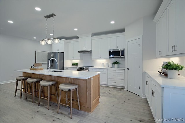 kitchen with white cabinetry, decorative light fixtures, a kitchen island with sink, and appliances with stainless steel finishes