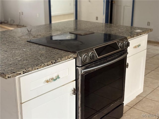 kitchen featuring electric stove, light tile patterned floors, dark stone counters, and white cabinets