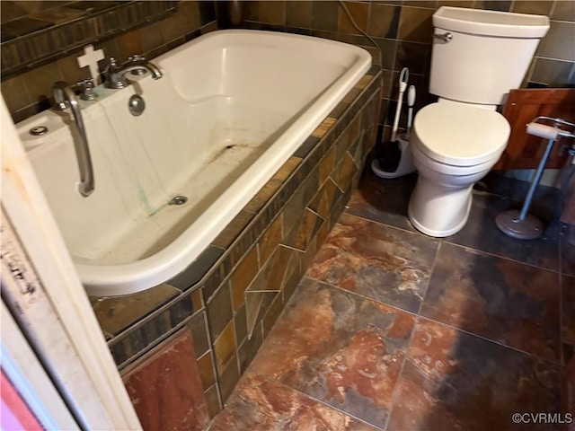 bathroom featuring tiled tub and toilet