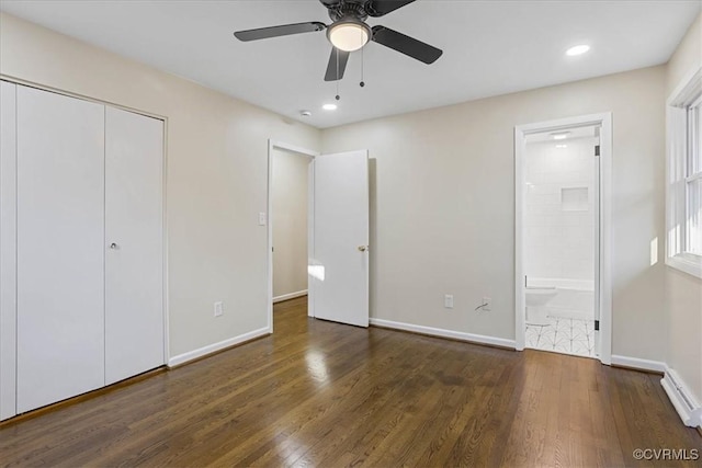 unfurnished bedroom with ensuite bath, ceiling fan, baseboard heating, dark hardwood / wood-style flooring, and a closet