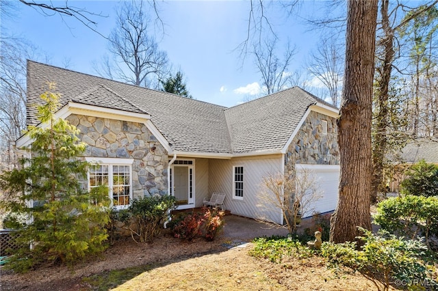 view of front facade with a garage, stone siding, and roof with shingles