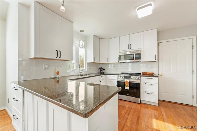 kitchen featuring appliances with stainless steel finishes, white cabinetry, sink, kitchen peninsula, and light wood-type flooring