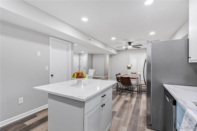 kitchen with stainless steel appliances, a kitchen island, light stone countertops, and white cabinets