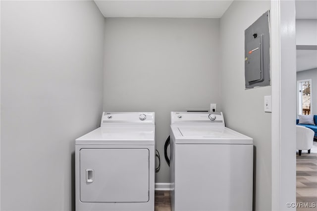 clothes washing area featuring washing machine and dryer, wood-type flooring, and electric panel