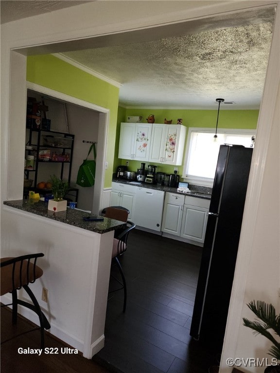 kitchen with white cabinets, a peninsula, a kitchen breakfast bar, freestanding refrigerator, and decorative light fixtures