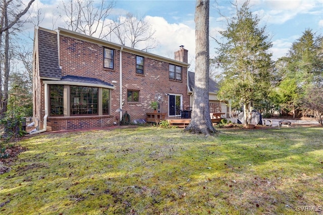 rear view of property featuring a deck, brick siding, roof with shingles, a lawn, and a chimney