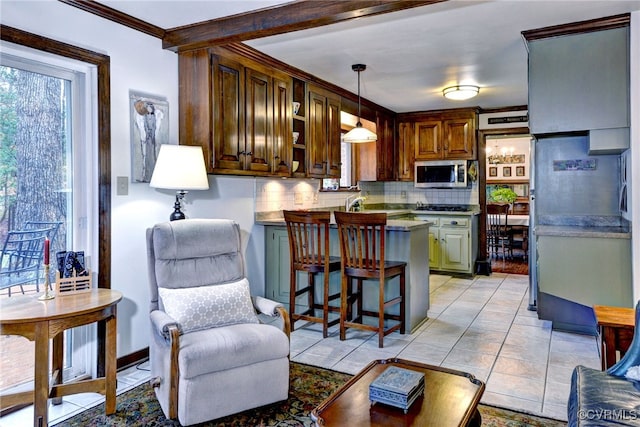 kitchen with a breakfast bar area, light tile patterned flooring, decorative backsplash, stainless steel microwave, and pendant lighting