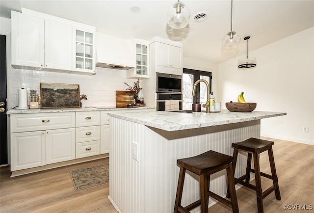 kitchen featuring white cabinetry, light stone countertops, a kitchen island with sink, and pendant lighting