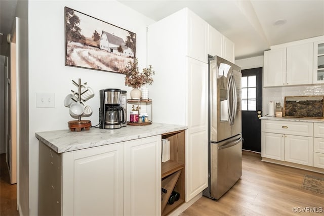 kitchen with light stone counters, stainless steel fridge with ice dispenser, light hardwood / wood-style flooring, white cabinets, and backsplash