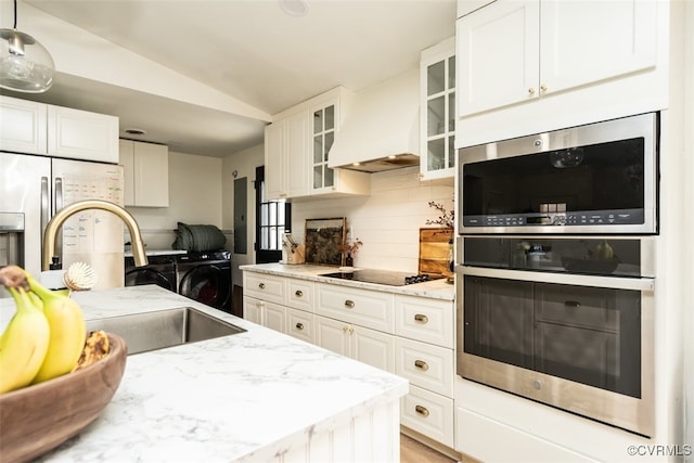 kitchen with white cabinets, custom exhaust hood, washing machine and clothes dryer, and appliances with stainless steel finishes