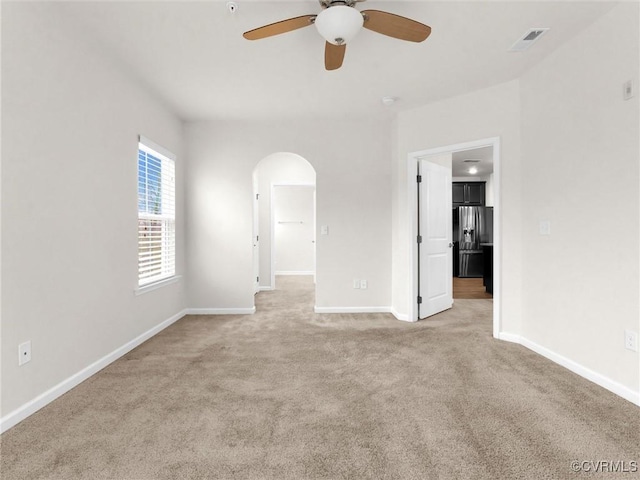 empty room featuring visible vents, a ceiling fan, arched walkways, baseboards, and light colored carpet