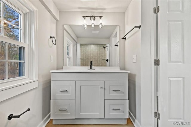 bathroom featuring a tile shower, vanity, and baseboards