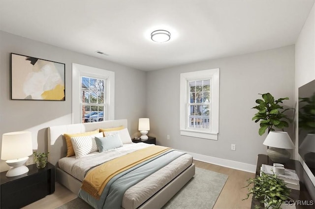 bedroom with multiple windows, wood finished floors, visible vents, and baseboards