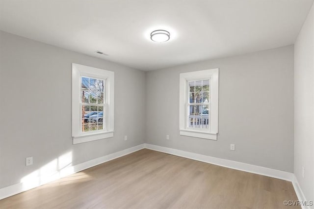 empty room featuring wood finished floors, visible vents, and baseboards