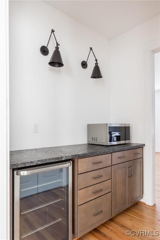 bar featuring light wood-type flooring, beverage cooler, stainless steel microwave, and a dry bar