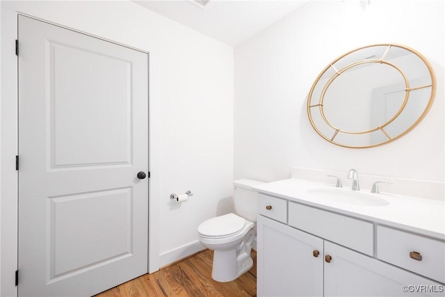 half bathroom with toilet, wood finished floors, and vanity