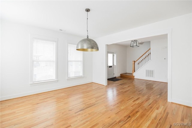 unfurnished dining area featuring stairs, light wood finished floors, visible vents, and baseboards