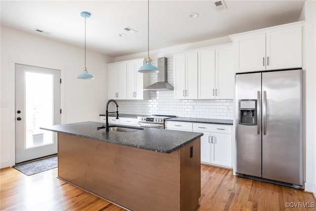 kitchen with dark countertops, wall chimney exhaust hood, appliances with stainless steel finishes, and a sink