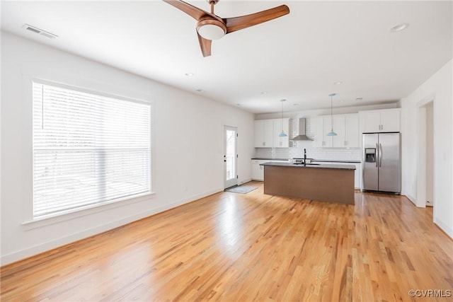 kitchen featuring white cabinets, wall chimney range hood, stainless steel fridge, and tasteful backsplash