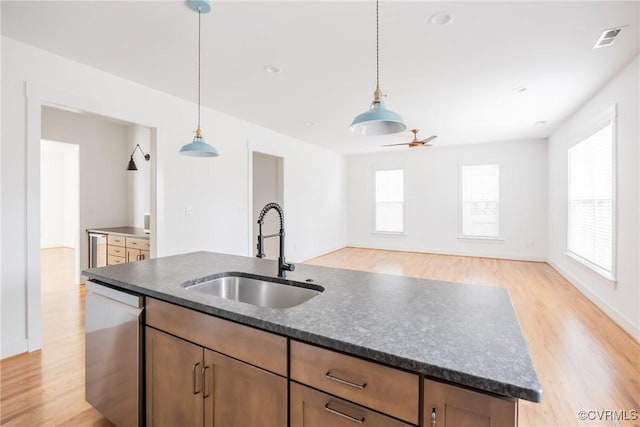 kitchen featuring visible vents, stainless steel dishwasher, light wood-style floors, a sink, and an island with sink