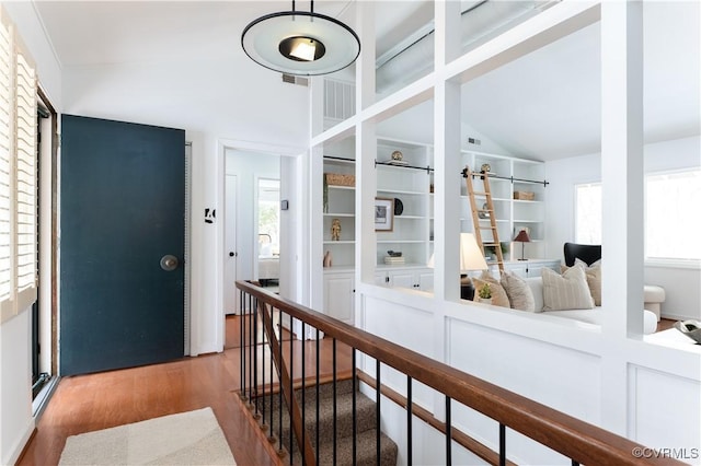 corridor with high vaulted ceiling, a barn door, wood finished floors, and visible vents