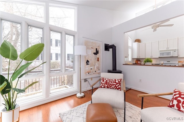 sitting room featuring high vaulted ceiling, a ceiling fan, baseboards, light wood finished floors, and a wood stove