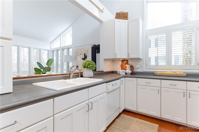 kitchen with white dishwasher, dark countertops, a sink, and white cabinets