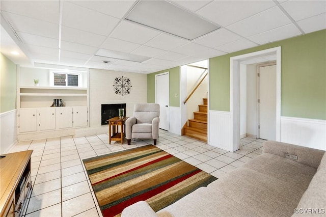 living room with a wainscoted wall, stairway, a fireplace with raised hearth, and light tile patterned flooring