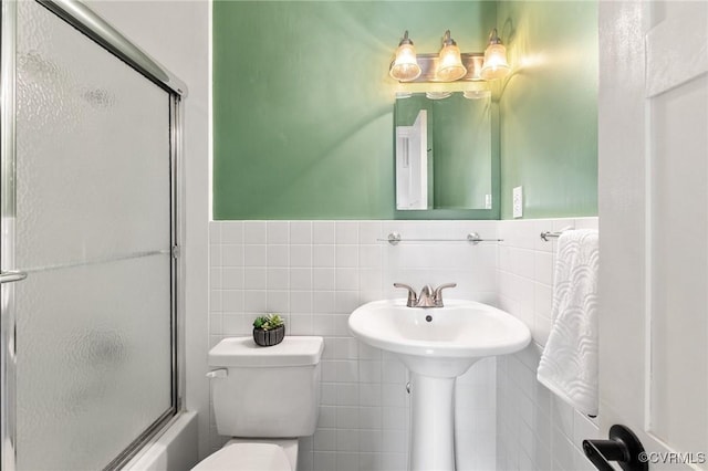 full bath featuring bath / shower combo with glass door, wainscoting, toilet, and tile walls