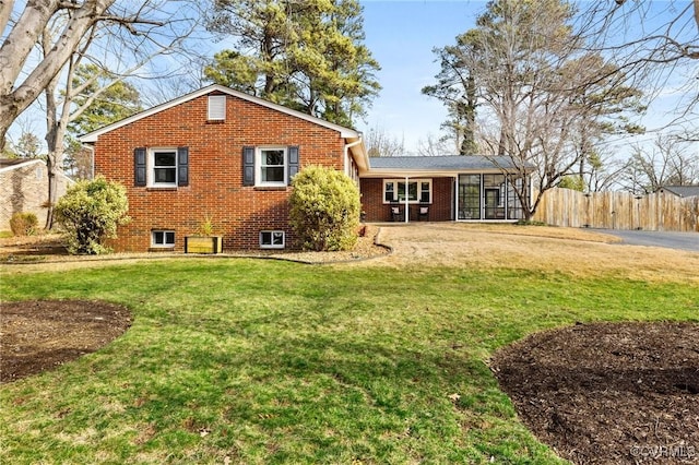 back of house featuring a yard, brick siding, fence, and a sunroom