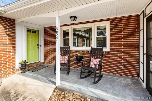 doorway to property featuring covered porch and brick siding