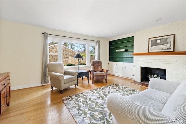 living room featuring a brick fireplace, built in features, light wood-style flooring, and baseboards