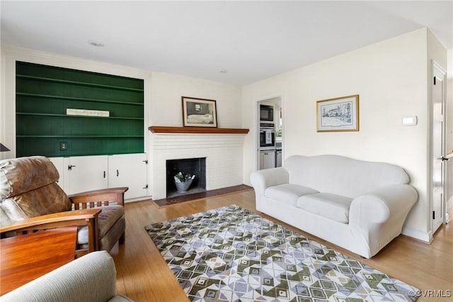 living room featuring built in shelves, a brick fireplace, and wood finished floors