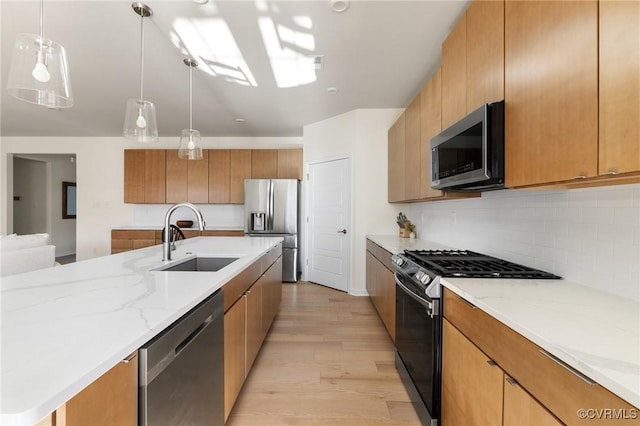 kitchen with a sink, light wood-style floors, appliances with stainless steel finishes, light stone countertops, and tasteful backsplash