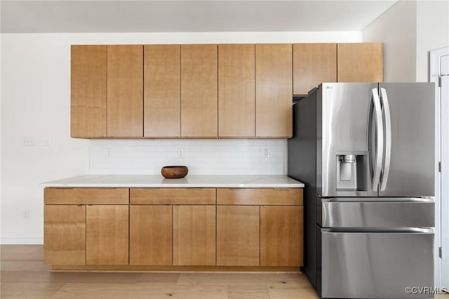 kitchen with brown cabinetry, stainless steel fridge with ice dispenser, light wood-style flooring, light countertops, and backsplash