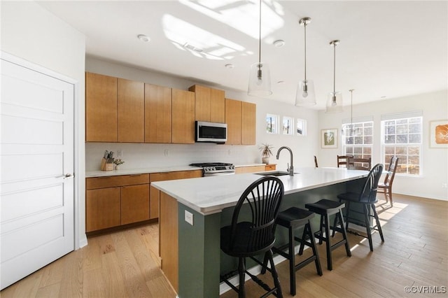 kitchen featuring a breakfast bar area, a sink, light countertops, appliances with stainless steel finishes, and light wood-type flooring