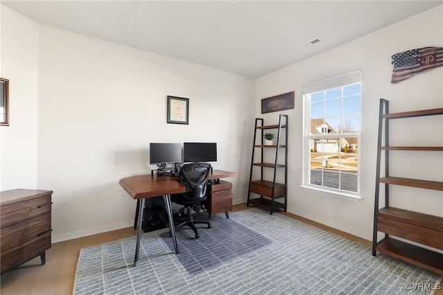 office space featuring baseboards, visible vents, and wood finished floors