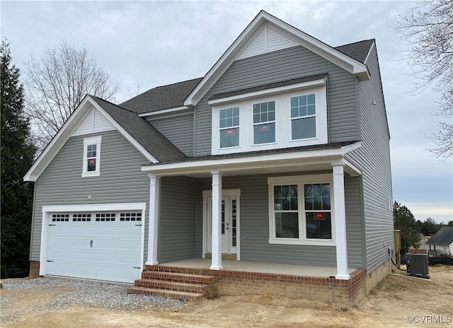 traditional-style house with a porch, central air condition unit, a garage, a shingled roof, and gravel driveway