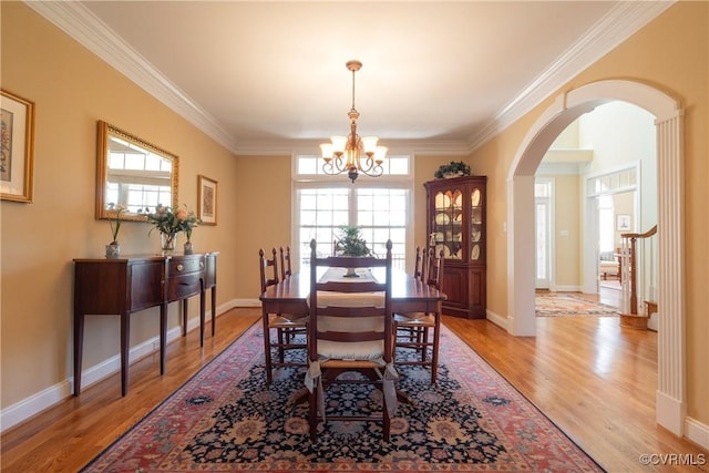 dining room featuring ornamental molding, arched walkways, a healthy amount of sunlight, and light wood-style flooring