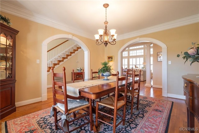 dining area with baseboards, arched walkways, ornamental molding, light wood-type flooring, and a chandelier