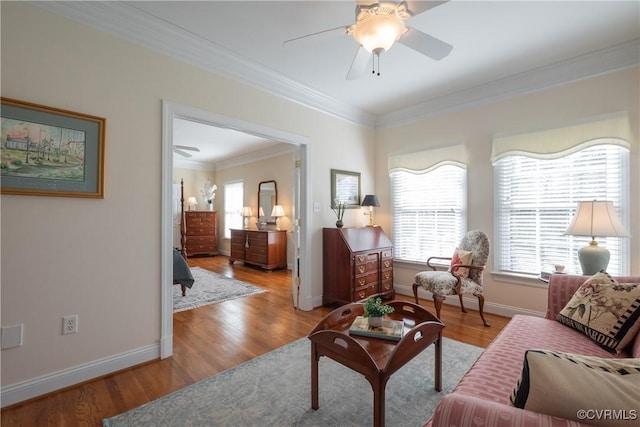 living area with ornamental molding, light wood-style floors, baseboards, and a ceiling fan