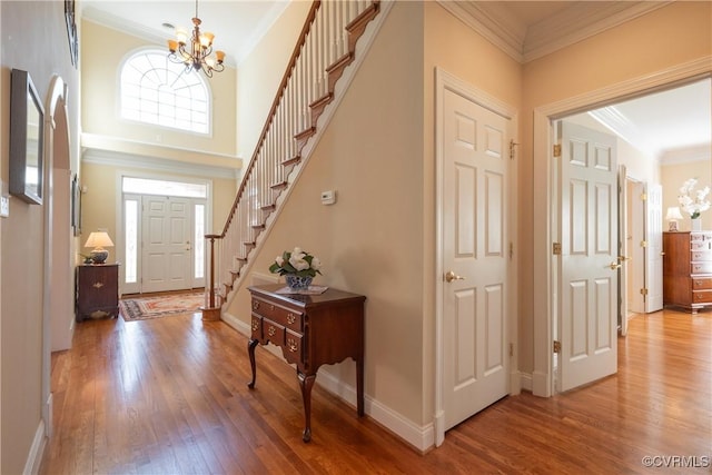 foyer featuring baseboards, ornamental molding, stairs, light wood-type flooring, and a notable chandelier