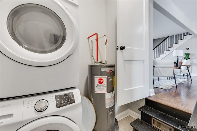 washroom featuring light tile patterned floors, water heater, stacked washer / dryer, laundry area, and baseboards