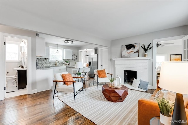 living area featuring a ceiling fan, a brick fireplace, and wood finished floors